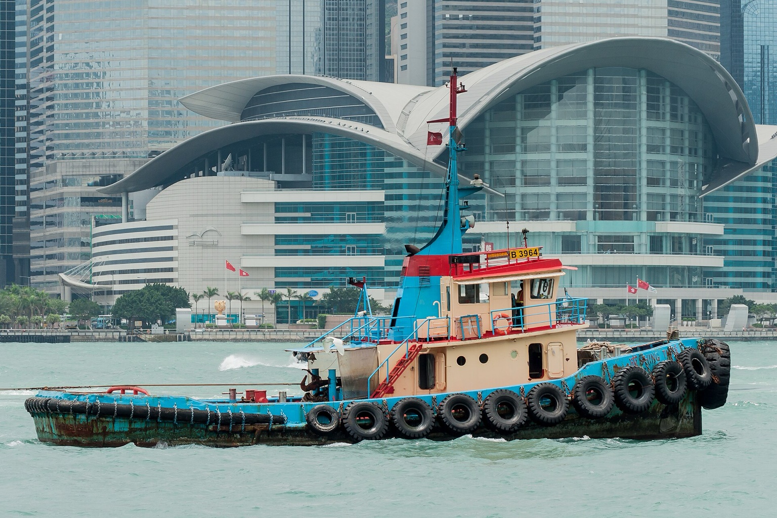 一艘拖轮驶过香港维多利亚港，背景是会议展览中心的弧形屋顶。
