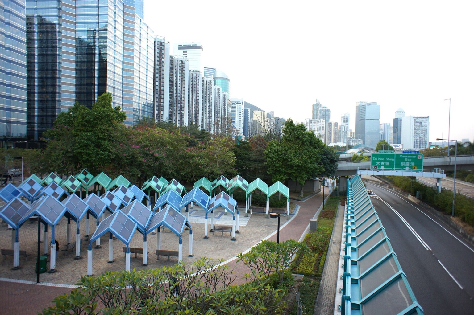 香港鰂魚涌公園的蓝绿色几何棚架，旁边是绿树、道路和太古城建筑。